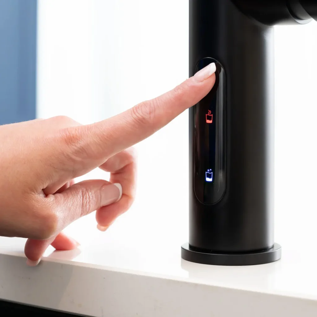 Finger pressing red hot water icon on matt black cylindrical tap control panel
