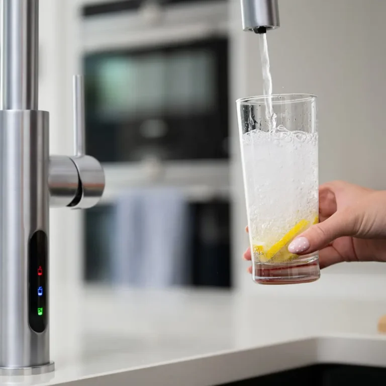 Brushed chrome C-shaped water tap filling glass with sparkling water and lemon slices