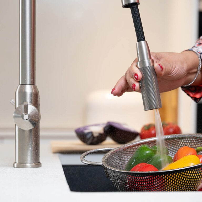 Quel Ultra Plus 4-in-1 instant boiling water tap in brushed nickel, pull-out spray rinsing fresh peppers in a colander.
