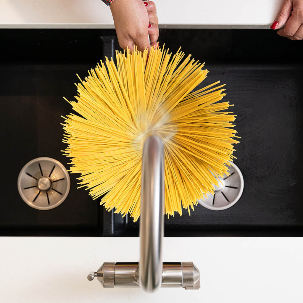 Quel Ultra Plus 4-in-1 instant boiling water tap in brushed nickel, overhead view of steaming hot water being used with spaghetti in the kitchen sink.