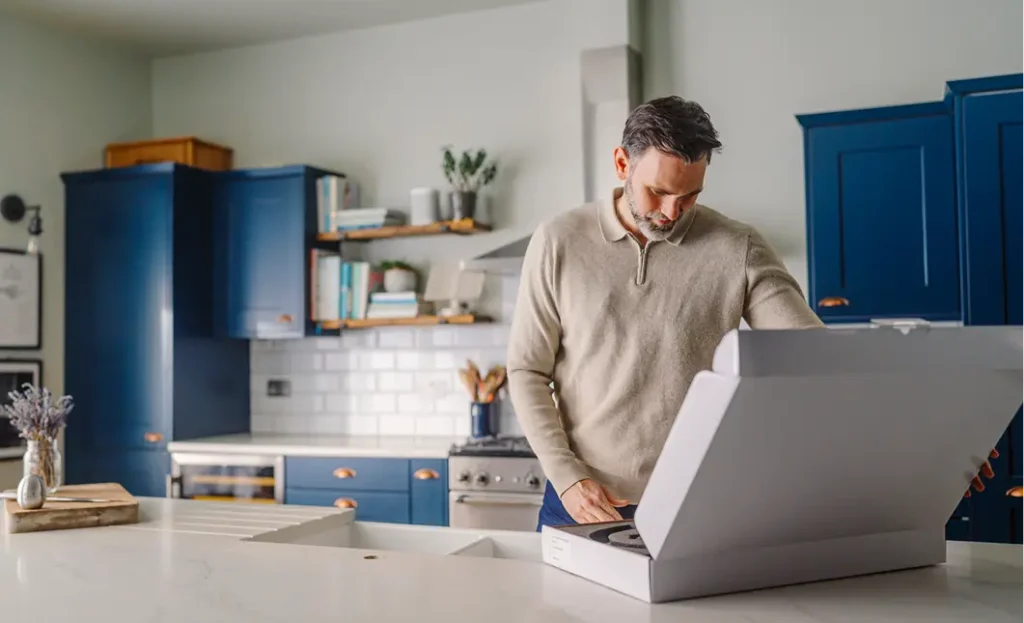 Man opening white box on white kitchen countertop with blue cabinets in background