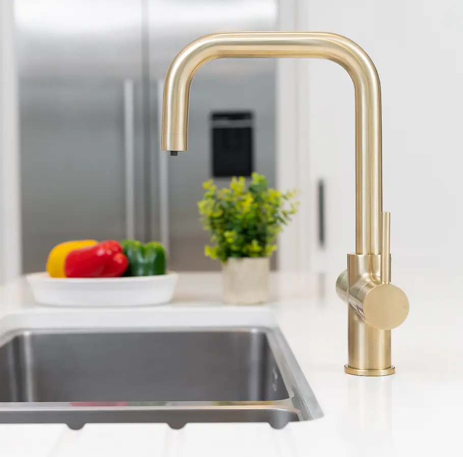 Modern gold-finished kitchen faucet with curved spout above stainless steel sink