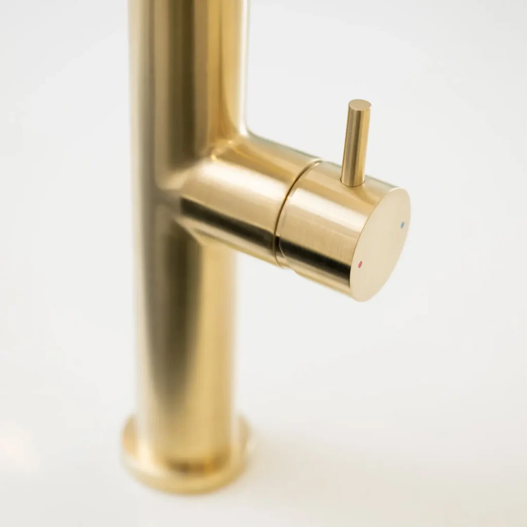 Close-up of the Quel Ultimo water tap body in brushed brass, showing the cylindrical side lever control with red and blue hot and cold indicator dots, against a plain white background